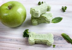 an apple and some dog treats on a wooden table next to it is a green apple