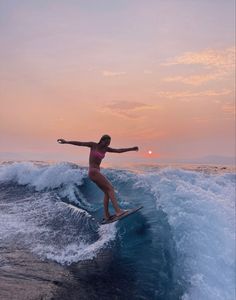 a woman riding a surfboard on top of a wave in the ocean at sunset