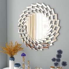 a mirror that is on the wall above a table with vases and flowers in front of it