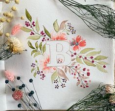 the letter b is surrounded by flowers and greenery on top of a piece of paper