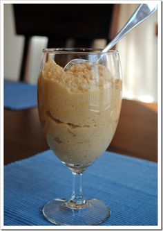 a dessert in a wine glass on a blue place mat with a spoon sticking out of it