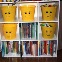 several yellow buckets with faces on them are sitting in front of a bookcase