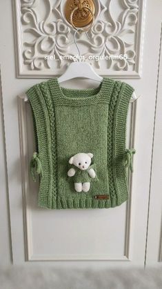 a green sweater with a teddy bear on it hanging from a hook in front of a door