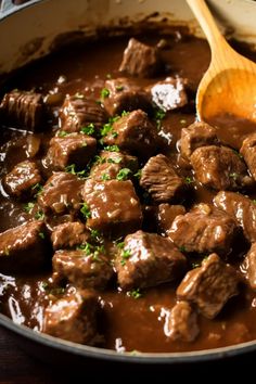 a pot filled with meat and gravy next to a wooden spoon