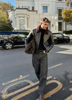 a man standing in the middle of an intersection wearing a leather jacket and jeans with his hands in his pockets