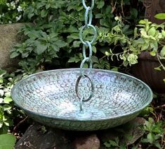 a metal bowl hanging from a chain in a garden