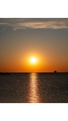 the sun is setting over the ocean with boats in the water and one boat on the horizon