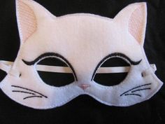 a white cat mask with black eyes on a black cloth background, showing the front part of it's face