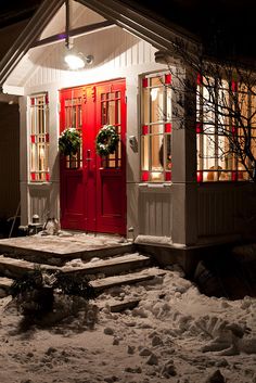 a red door and steps in front of a white house with snow on the ground