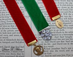 two red, green and gold ribbons are laying on top of an open book with a medal