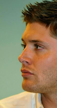 a close up of a man with short hair wearing a white shirt and earring