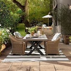 an outdoor dining area with wicker furniture and potted plants on the side walk