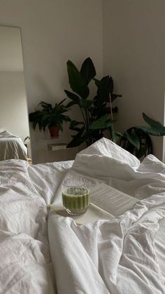 an unmade bed with white sheets and a green drink on the pillow next to it