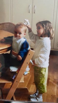 two young children standing in front of a wooden table with chairs on top of it