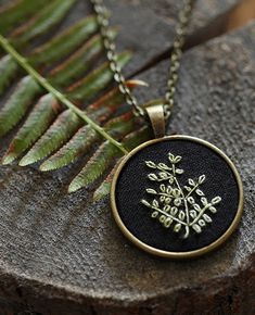 a black and gold embroidered pendant on a wooden surface with fern leaves in the background