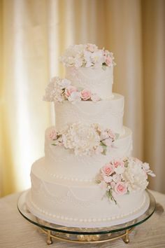 a three tiered wedding cake with pink flowers on the side and white icing