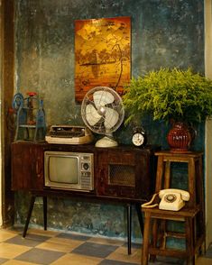 an old fashioned television sitting on top of a wooden table next to a fan and plant