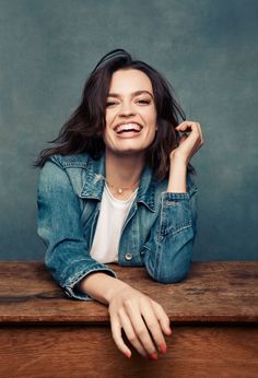 a smiling woman sitting at a table with her hands on her head and arms crossed