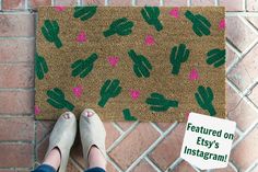 a person standing in front of a door mat with pink and green cactus designs on it