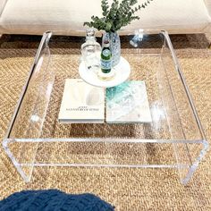 a glass coffee table with two bottles on it and a plant in the centerpiece