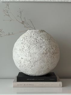 a white vase sitting on top of a stack of books next to a framed picture