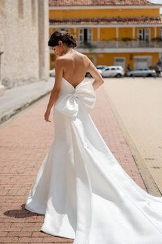 a woman in a white wedding dress is walking down the street with her back to the camera