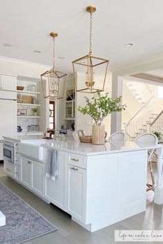 a kitchen with white cabinets and an island in front of the sink, has gold hanging lights above it