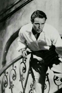 a man leaning on the hand rail of a stair case while wearing a shirt and tie