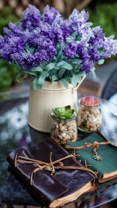 purple flowers are in a pot next to an open book on a table with other items