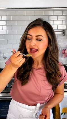 a woman in a pink shirt is eating food from a spoon with her mouth open