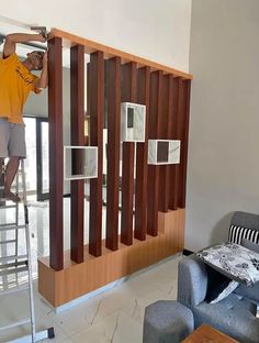 a man standing on a ladder in front of a living room with wooden slats