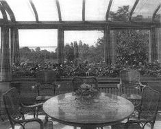 an old black and white photo of a dining room table with chairs in front of large windows