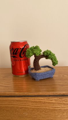 a crocheted bonsai tree sits next to a can of coca - cola