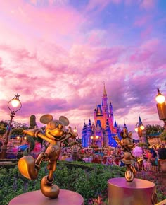 the mickey mouse statue in front of disney's castle at dusk with pink and blue sky