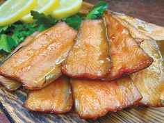 sliced up fish sitting on top of a wooden cutting board next to lemon wedges