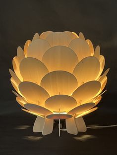 a large white flower shaped lamp on a black surface with the light reflecting off it's petals