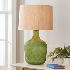 a green vase sitting on top of a white table next to a book and lamp