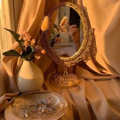 a vase filled with flowers next to a mirror on top of a table covered in cloth