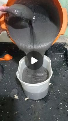 a person pouring water into a bucket on top of a black table with orange utensils