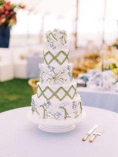 a three tiered cake sitting on top of a white table covered in blue and green flowers