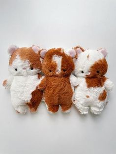 three small stuffed animals sitting next to each other on a white surface with one cat in the middle