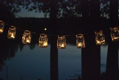 mason jar lights strung from a string in the dark with trees and water in the background