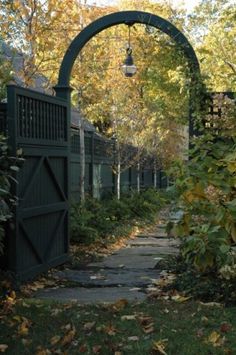 a street light hanging over a sidewalk next to trees and bushes with leaves on the ground