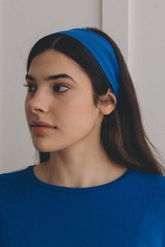 a woman wearing a blue headband looking off to the side in front of a white wall