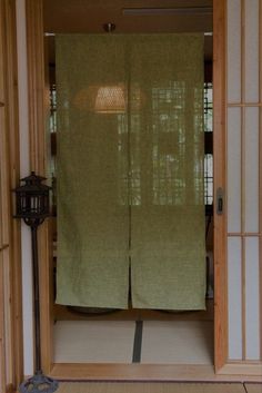 an open door with two green curtains on the inside and outside, in front of a lamp