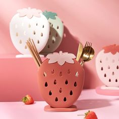 three strawberries with forks and spoons in the shape of utensils on a pink surface