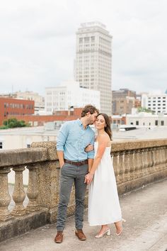 a man and woman standing next to each other on a bridge in front of tall buildings