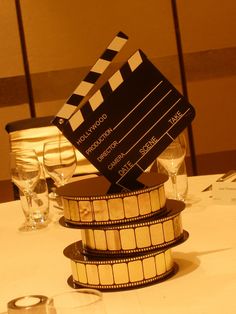 a table topped with a stack of film reels next to wine glasses and silverware