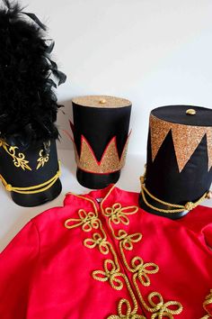 three hats are sitting on top of a red cloth and one is black with gold trim