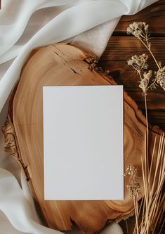 an empty white card sitting on top of a piece of wood next to dried flowers